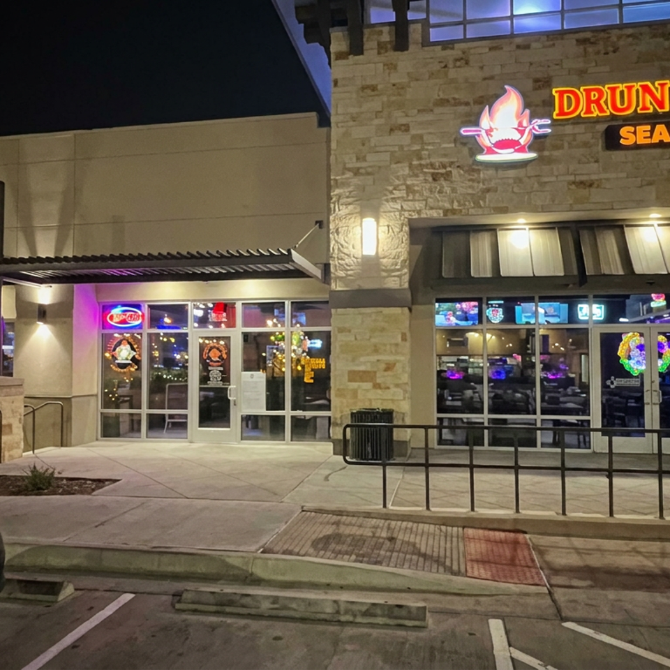 Nighttime exterior of Drunken Crab Seafood Bar, showing illuminated signage, storefront windows, entrance, and sidewalk.