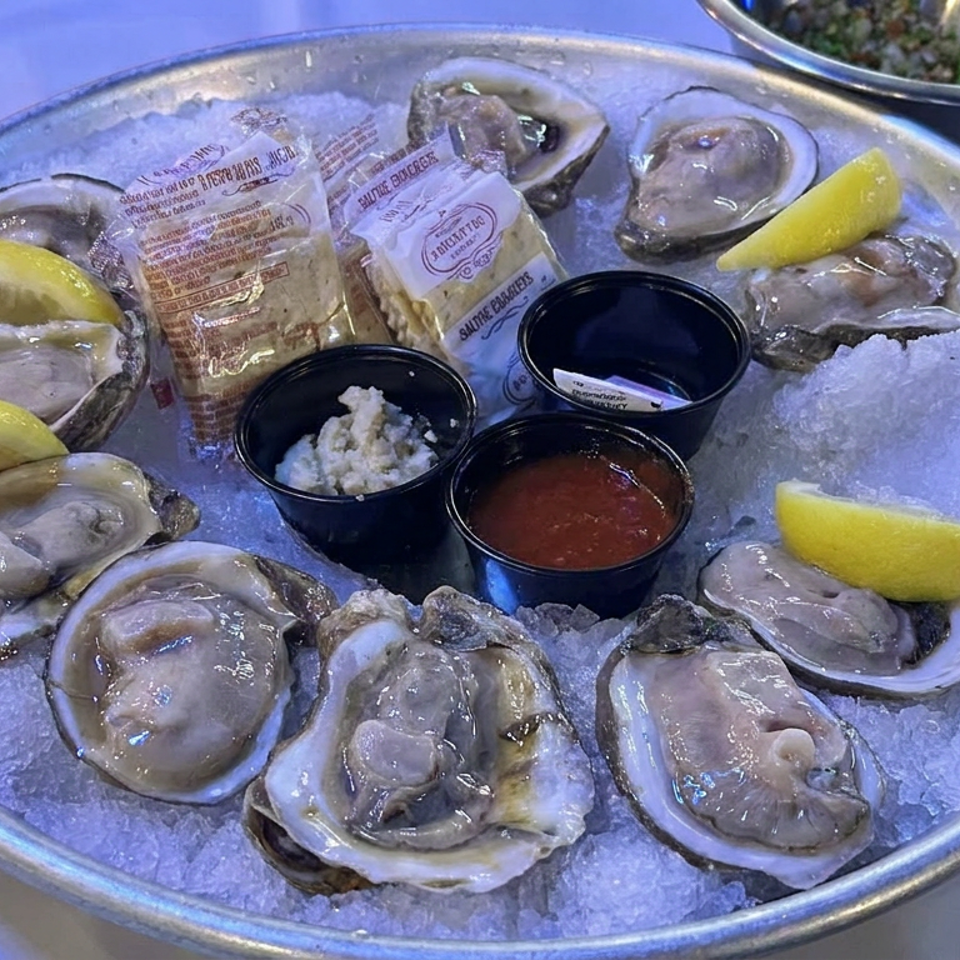 Platter of raw oysters on crushed ice with lemon wedges, cocktail sauce, horseradish, and condiment packets.